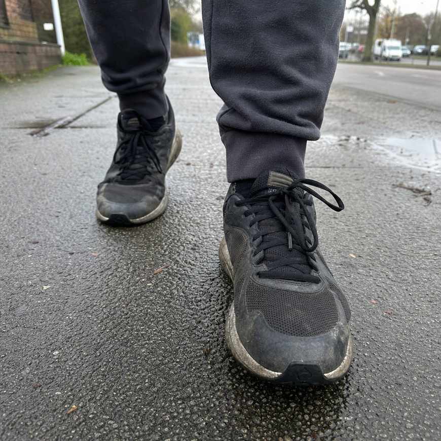 Close-up of a runner's trainers on a grey suburban pavement, mid-stride at an easy walking pace