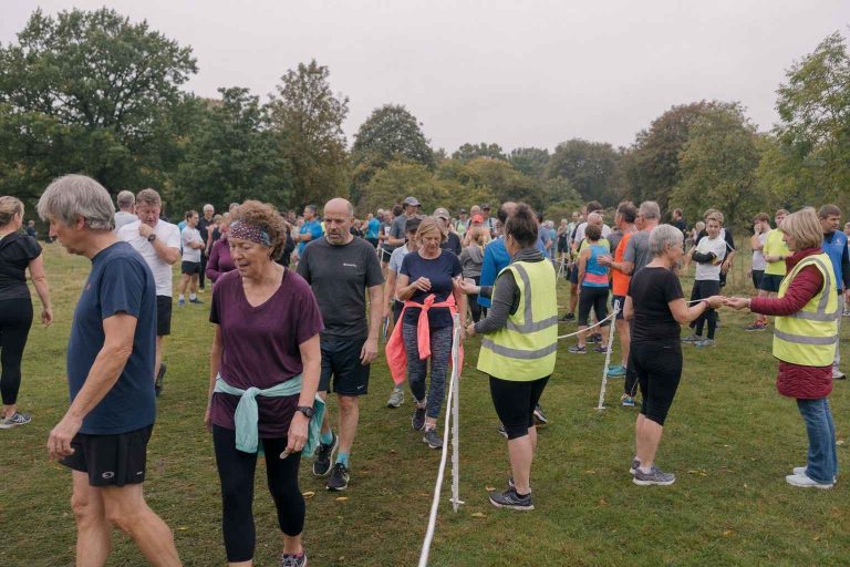 A group of everyday runners and walkers crossing a parkrun finish line on a grey Saturday morning in a UK park