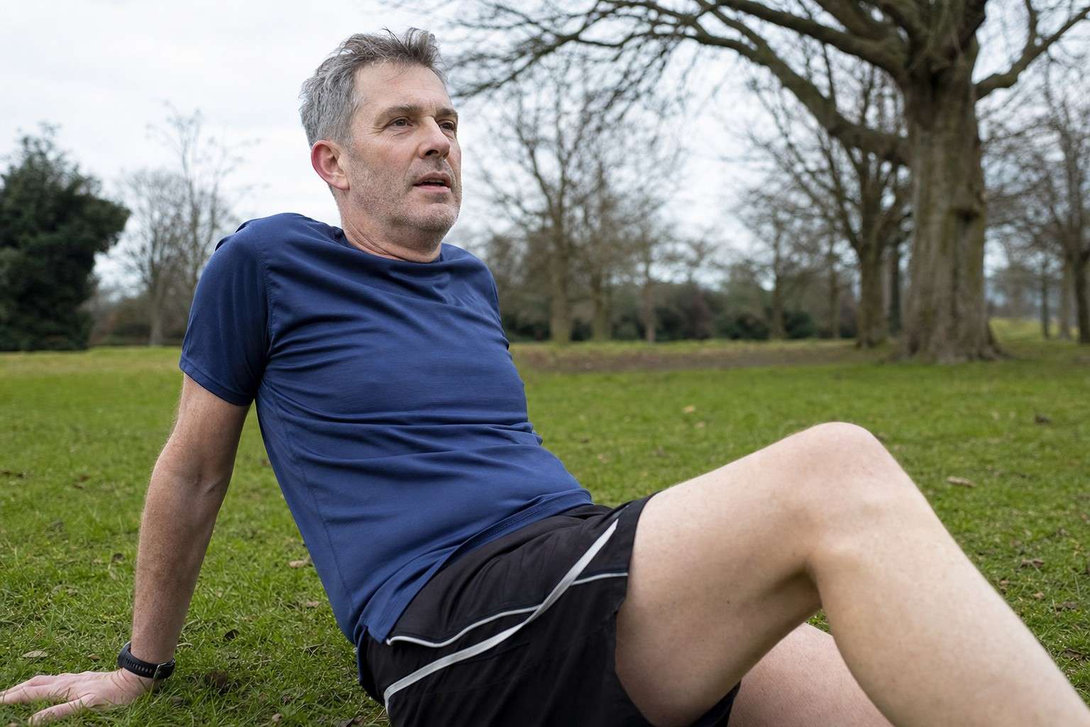Low close-up of a runner resting back on the grass in a park after a run, relaxed