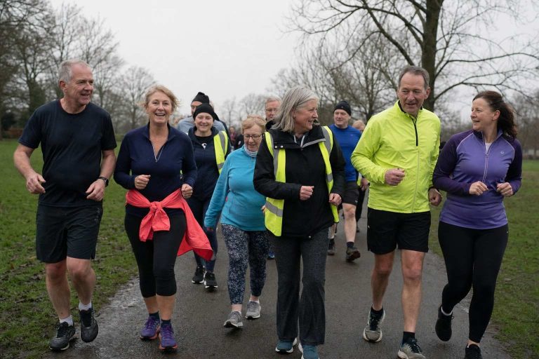 A small mixed-age group of runners and walkers setting off together at a parkrun on a grey morning